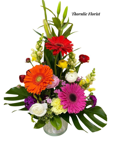 Vibrant garden pot with red, orange, and pink gerbera daisies and white ranunculus.