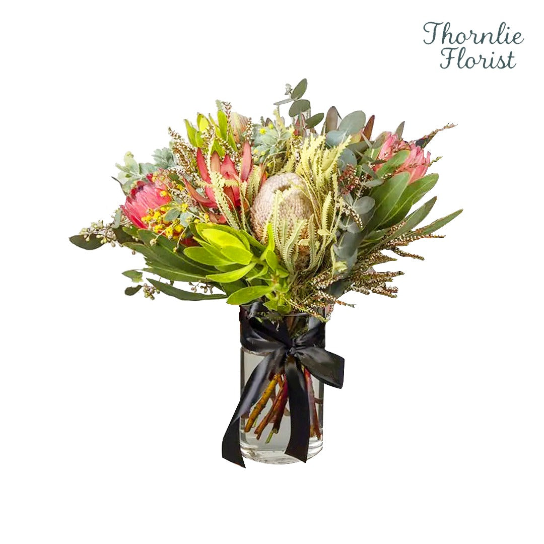 Native floral arrangement with proteas and eucalyptus in a glass vase by Thornlie Florist